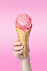 Woman's hand holding waffle cone with strawberry ice cream on pink background food