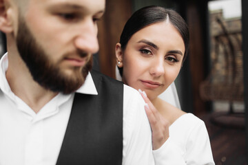 A man and a woman are standing close to each other, with the woman looking at the camera. The man is wearing a suit and the woman is wearing a wedding dress. Scene is romantic and intimate