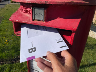 An Envelope B for the United Kingdom General Election postal vote can be seen with a hand putting it in a red post.First Class box.