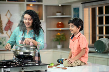 Elegant Mother Cooking In Kitchen And Her Son Watching Her