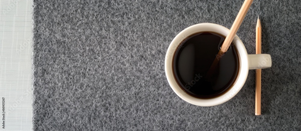 Poster bird's-eye view of a white coffee mug and pencil on a gray felt desk pad with a clear space for imag