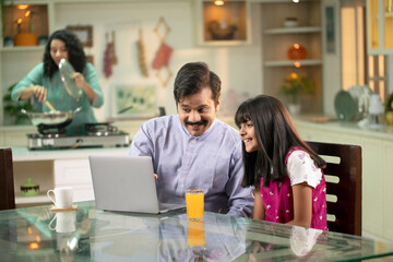 Father Daughter Surfing Internet With Laptop On Table At Kitchen