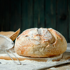 fresh loaf of bread sprinkled with flour on a wooden background