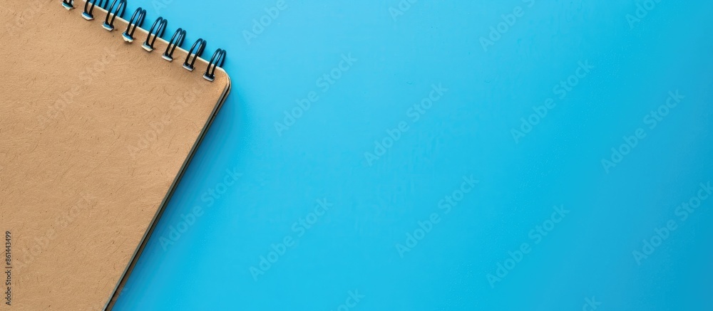 Poster Close-up of a spiral-bound notebook with brown blank pages against a blue backdrop, with copy space image.