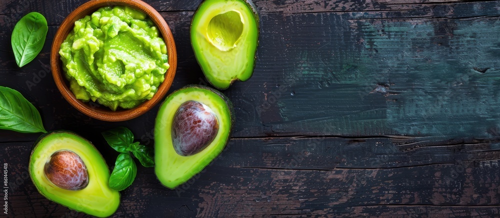 Poster close-up top view of half and whole avocadoes with guacamole sauce, set on a dark wood background, l