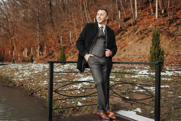 Fototapeta premium A man in a suit and tie stands on a bridge overlooking a body of water. He is smiling and he is enjoying the view