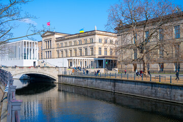Clear skies over the New Museum with visitors walking along the riverbank in Berlin, Germany.