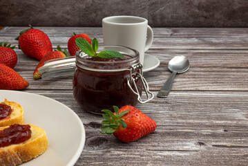 Table set with homemade strawberries and mint jam for a sweet breakfast. Glass jar with strawberries jam and mint leaves