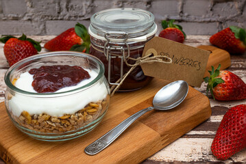 Glass jar full of muesli and yogurt with homemade strawberries jam, delicious snack with cheesecake and strawberries jam on wooden cutting board, detail with vintage cardboard tag