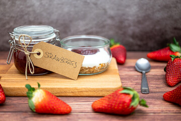 Glass jar full of muesli and yogurt with homemade strawberries jam, delicious snack with cheesecake and strawberries jam on wooden cutting board, detail with vintage cardboard tag