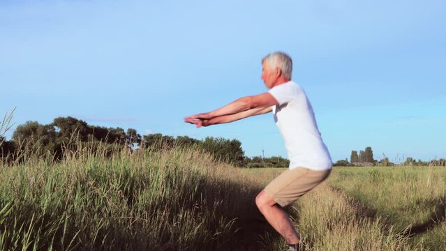 Active pensioner doing outdoor exercises in the meadow to stay fit and enjoy nature regular physical activities squatting in the field during the summer