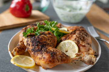 Roasted chicken legs on a plate with lemon and parley garnish. Served ready to eat on a table