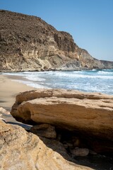 Fototapeta premium Scenic view of a rocky beach with waves crashing on the shore under a clear blue sky.