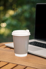 Cup of coffee and laptop on the table on a blurred background of the forest.