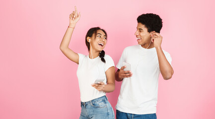 Happy students dancing and listening music by earphones over pink studio background