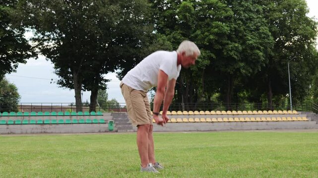 Mature athlete man staying healthy by participating in regular exercises and stretches at the stadium focusing on physical well-being doing workout outdoor