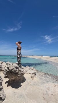 Solo woman traveler. Formentera beach. Young woman enjoying the view on the beach. Beautiful turquoise water and an empty beach.