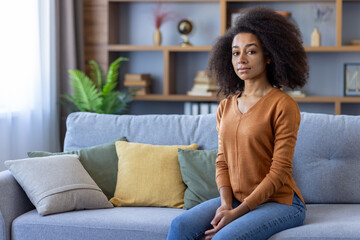 Confident young woman sitting on couch in modern living room with stylish decor. Relaxed and calm atmosphere. Natural light creating cozy ambiance.