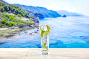 Glass of icy mineral water with mint leaves on wooden  table and copy space for drinks and food and products. Seascape in summer background.