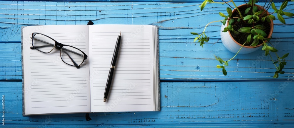 Poster a top-down view of an open notebook, pen, glasses, plant on a blue wooden surface with a blank area 