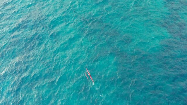 Outrigger Canoe rowing on turquoise blue sea in Hawaii overhead top down aerial drone shot of sport activity. Hawaiian outrigger paddling and canoes