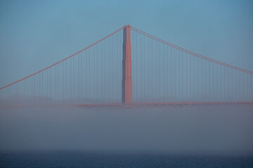 World famous red steel suspension bridge in San Francisco port entrance with Golden Gate State park nature lands hidden in cloud mist fog bank with clear sky pilars