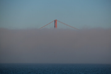 World famous red steel suspension bridge in San Francisco port entrance with Golden Gate State park nature lands hidden in cloud mist fog bank with clear sky pilars