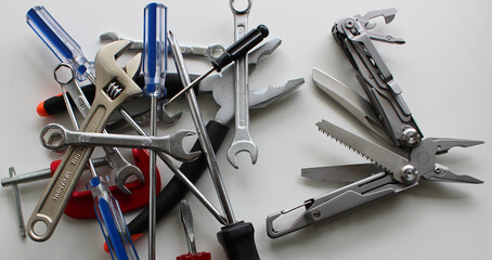 Half-opened full metal multi-tool with different blades and stacked multi-colored tools on a white table
