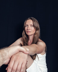 Fototapeta premium Attractive woman giving hand to man on black background. Support, looking into camera, long hair.