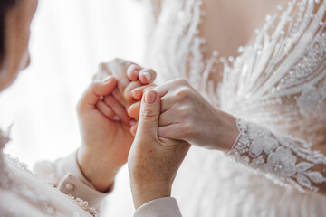 The daughter, who has become a bride, tenderly holds her mother's hands. The bride's mother blesses the bride for a happy family life.