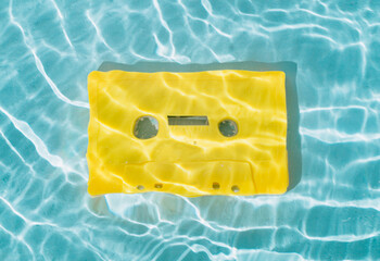 Summer scene with yellow audio cassette tape in water. Sun and shadows. Summer retro music concept....
