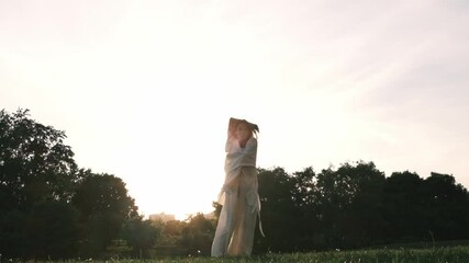dancer in white robes moves gracefully with arms raised against the backdrop of a setting sun. This scene reflects the beauty and fluidity of dance in the natural environment.