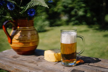 valmiera, Latvia - September 15, 2023 - A glass of beer and a piece of cheese on a wooden table, next to a vase of blue flowers, celebrating Midsummer in Latvia.