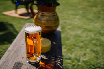 valmiera, Latvia - September 15, 2023 - A glass of beer on a wooden table with cheese and a traditional Latvian vase in the background, celebrating Midsummer outdoors.