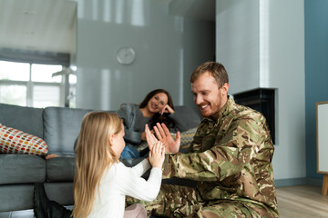 Rejoicing soldier man playing with cute little daughter at home