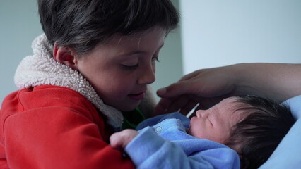 Young boy gently holding newborn baby in blue outfit, emotional and tender family moment,...
