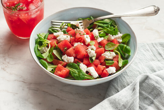 Watermelon light summer salad with lettuce, young goat cheese, watermelon and spices, served with watermelon smoothie. Light summer recipes, dietary fruit salads. Sunlight, white table,  frot view