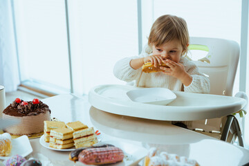 Little child eating eclair, in front of a table with lots of sweet food. 
