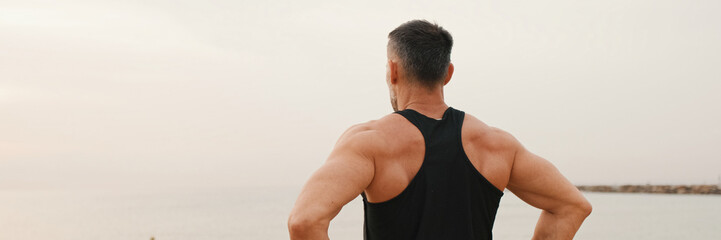 Mature man doing warm up before workout while standing on the beach, Back view, panorama