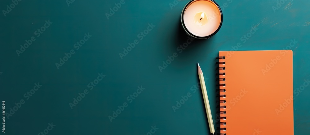 Poster top-down view of an open notebook with lined paper, a black pencil, and orange candles on a blue-gre