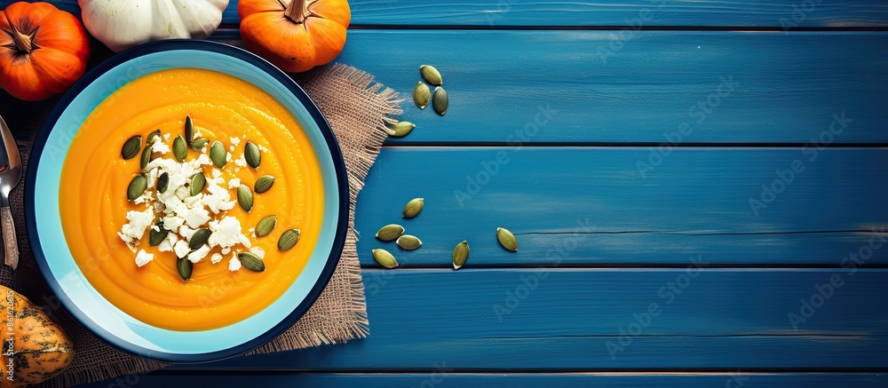 Poster a top view of pumpkin soup puree served in a blue plate on a wooden table. decorated with slices of 