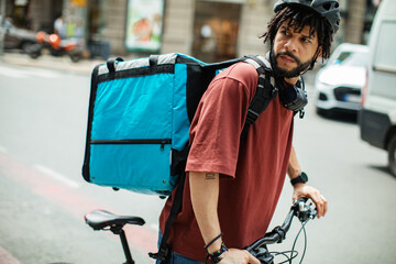 Delivery man with large backpack riding bicycle in urban setting