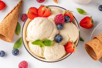 White ice cream bowl with vanilla gelato and fresh berries. Big portion of classic vanilla taste ice cream, with strawberry, raspberry, blueberry, blackberry, and waffle ice cream cones