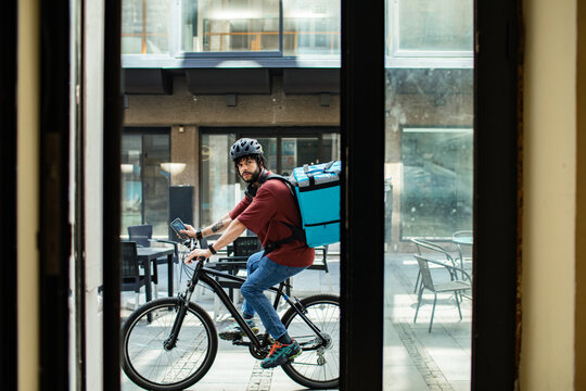 Delivery man with large backpack riding bicycle in urban setting