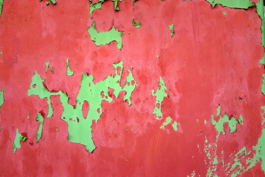 A wall with green and red paint peeling off