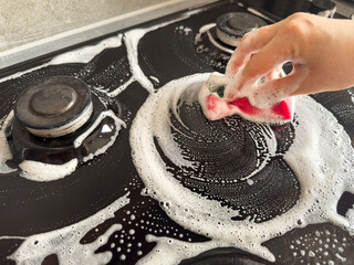 Hands cleaning gas cooker with special white foam in the kitchen