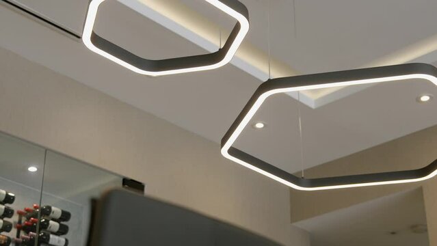 Modern interior lighting fixture with geometric design. Two interconnected shapes decoration resembling hexagons with rounded corners emitting bright white light