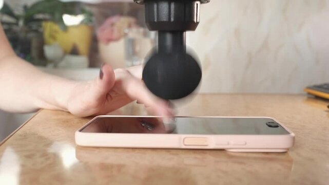 Close up of woman's hands quickly presses her fingers on smartphone screen using percussion massager, earning virtual crypto coins. Taping for online earning of tokens. Crypto app and farming, online 