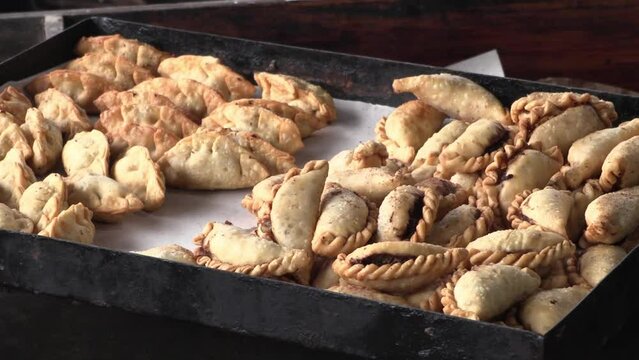Tray with freshly cooked fried empanadas. Cook taking out hot Creole empanadas for sale. Traditional Argentine food. Typical food of Argentina.