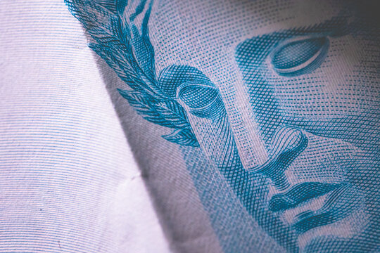 Uma nota de 100 reais com dobra em ambiente escuro em fotografia macro. Real, moeda brasileira. Economia do Brasil, infla&ccedil;&atilde;o e crise financeira.